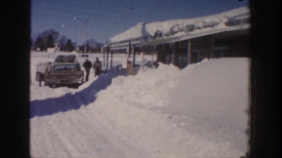 Aspen, Colorado 1961 frame showing a station wagon with luggage on top as two adults stand beside deep winter snow.