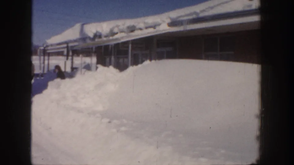 Aspen, Colorado 1961 home-movie frame showing deep snow beside a low building, with a person partly visible at left.