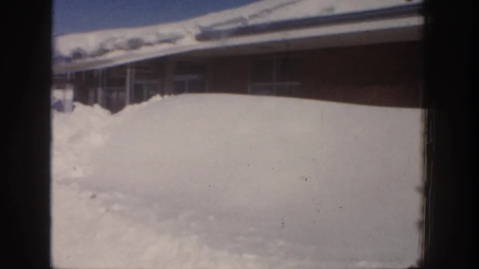 Aspen winter frame from 1961 showing a high snow drift against a low building with roof snow and visible film wear.