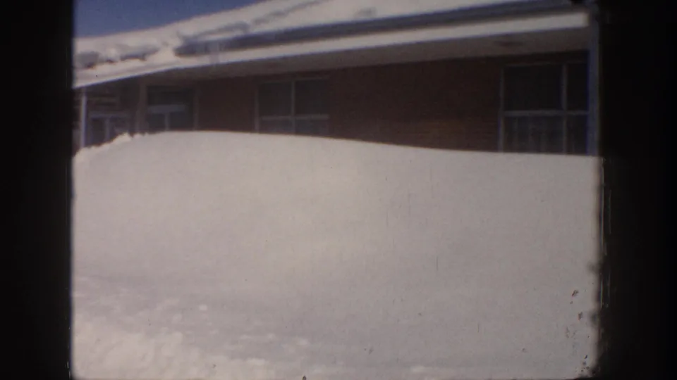 1961 Aspen home-movie frame with a close view of deep snow piled against a low building and dark window openings.
