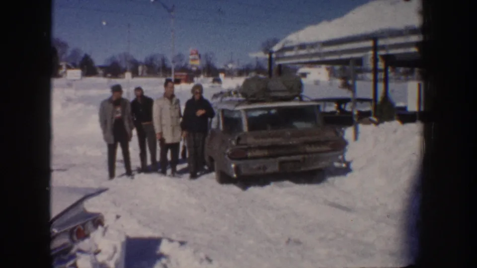 Aspen, Colorado 1961 frame showing four bundled men beside a tail-finned station wagon with luggage on the roof.