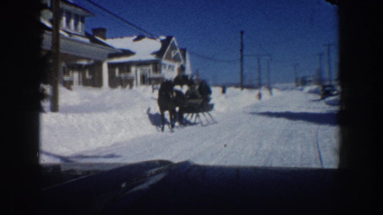 The sleigh travels through a snow-covered Aspen residential street in 1961, framed from inside a vehicle under a clear blue sky.