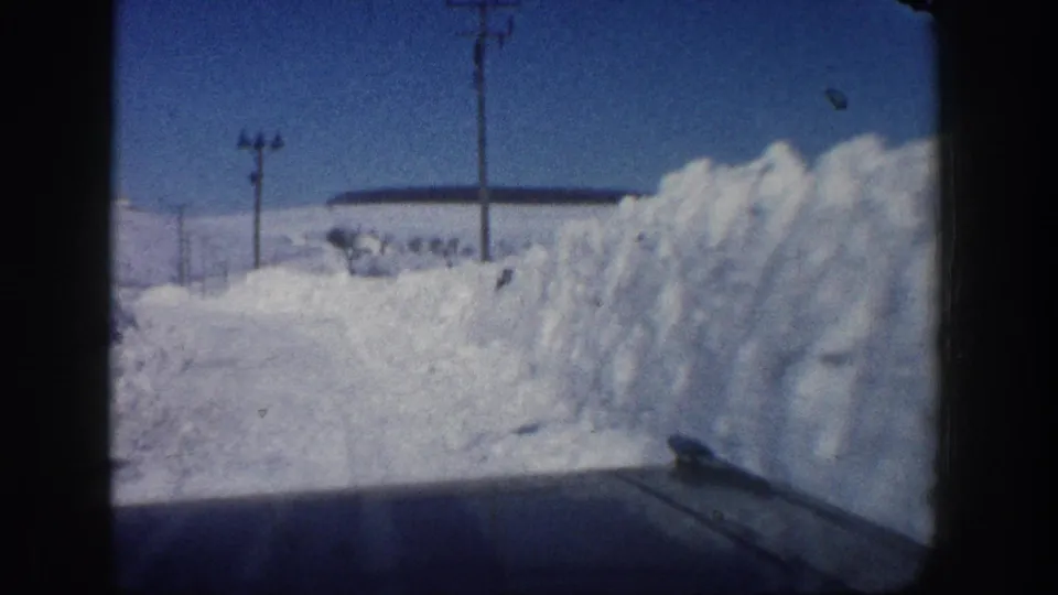 1961 Aspen, Colorado home-movie view from inside a car on a narrow snow-covered road lined by high plowed banks and utility poles.