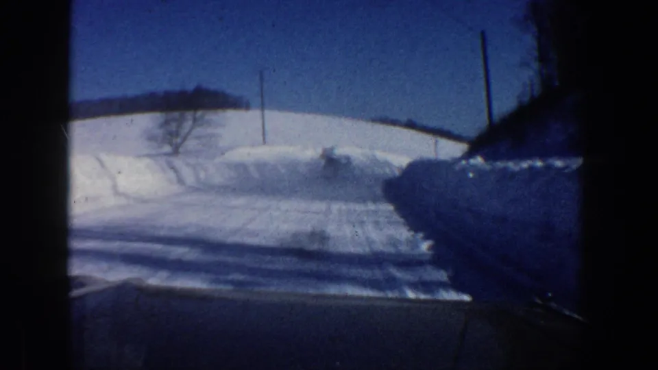 1961 Aspen-area winter road seen from inside a moving car, with snowbanks, utility poles, and blue sky.