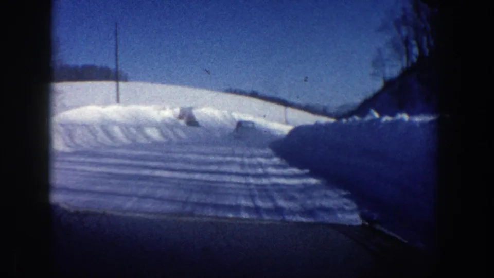 Interior windshield view of a snowy Aspen road in 1961, showing deep roadside snow and winter light.