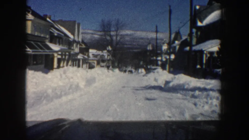 From inside a car, the 1961 Aspen footage shows a narrow winter street, snow-covered houses, roadside piles, and distant mountains.