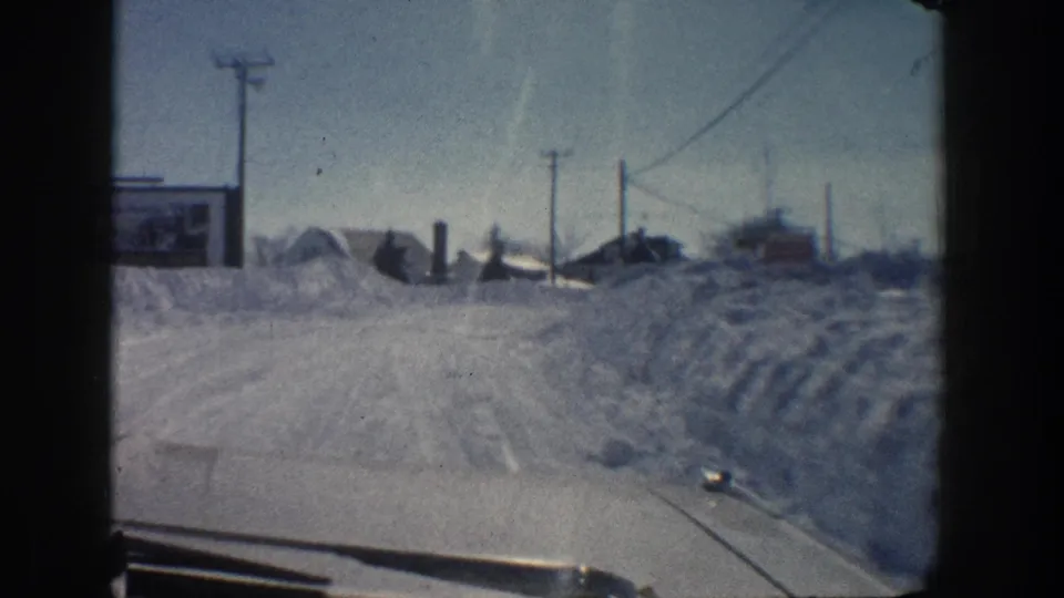 End of the 1961 Aspen vehicle-view clip, with snowbanks, utility lines, low structures, and winter road texture visible ahead.