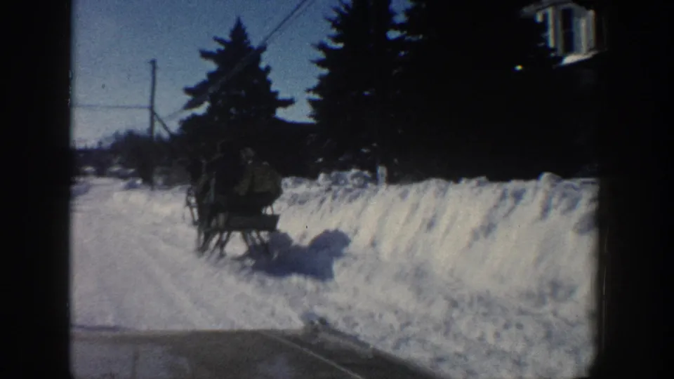 A horse-drawn sleigh with visible passengers passes along a snowy Aspen road in the 1961 8mm home-movie footage.