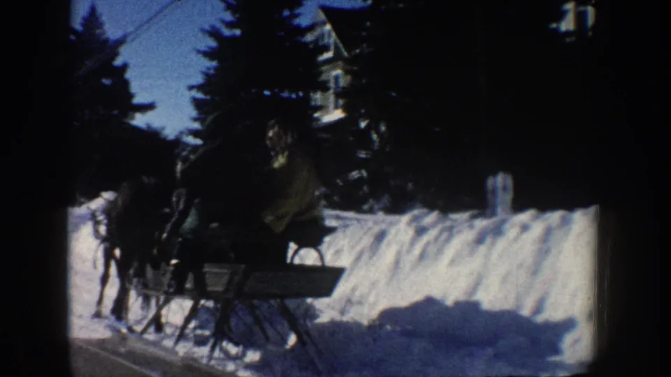 The passing sleigh and horse are seen closer against tall snowbanks and evergreens in this Aspen winter street view.