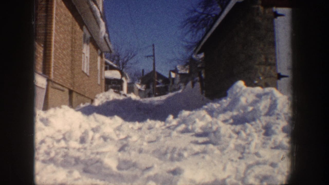 Snow-covered residential alley between buildings under a clear blue sky.