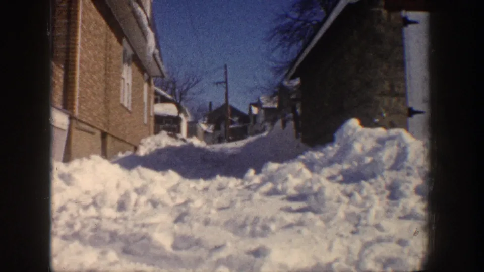 1961 Aspen, Colorado 8mm frame showing deep snowdrifts in a narrow residential alley beside brick buildings.