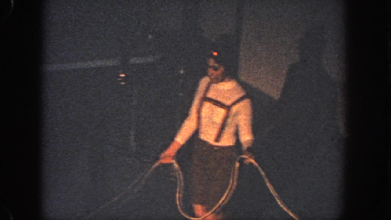 One swimmer stands in dark water holding a rope with a dim wall behind her.