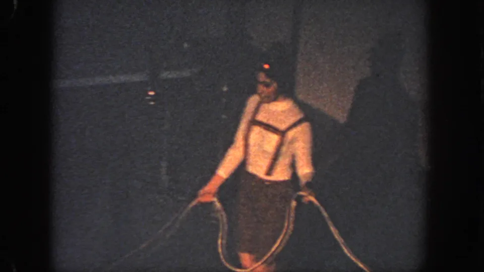 A swimmer in a white top and dark shorts holds a rope line in dim 1951 Atlanta pool footage.