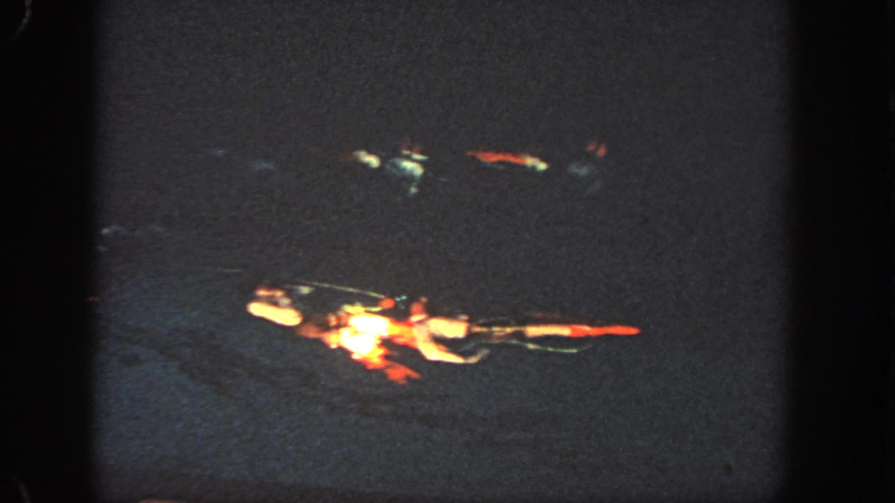 1951 Atlanta home-movie frame showing distant swimmers in red and white suits crossing dark water during a nighttime aquatic performance.