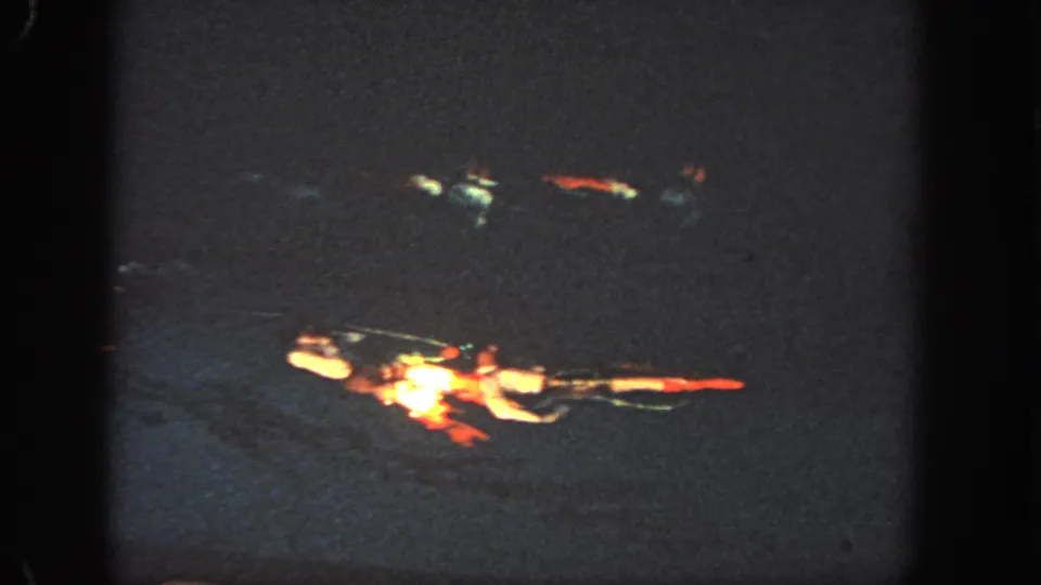 1951 Atlanta home-movie frame showing distant swimmers in red and white suits crossing dark water during a nighttime aquatic performance.