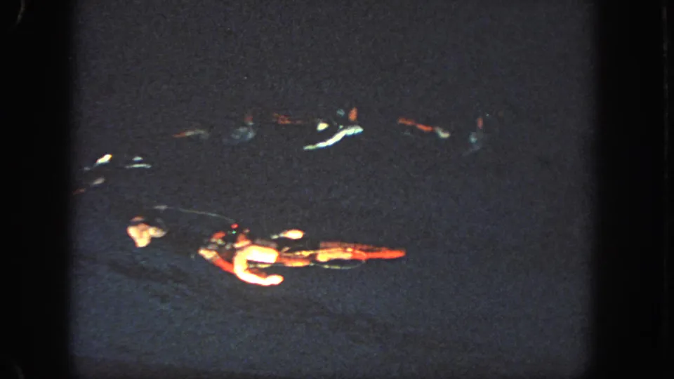 1951 Atlanta footage shows swimmers in a loose nighttime formation, partly illuminated against nearly black water.