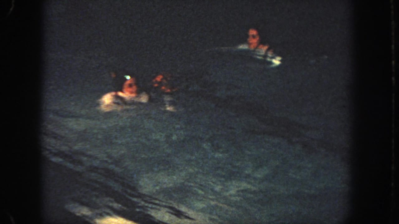 Several swimmers move through a dark pool under dim light.