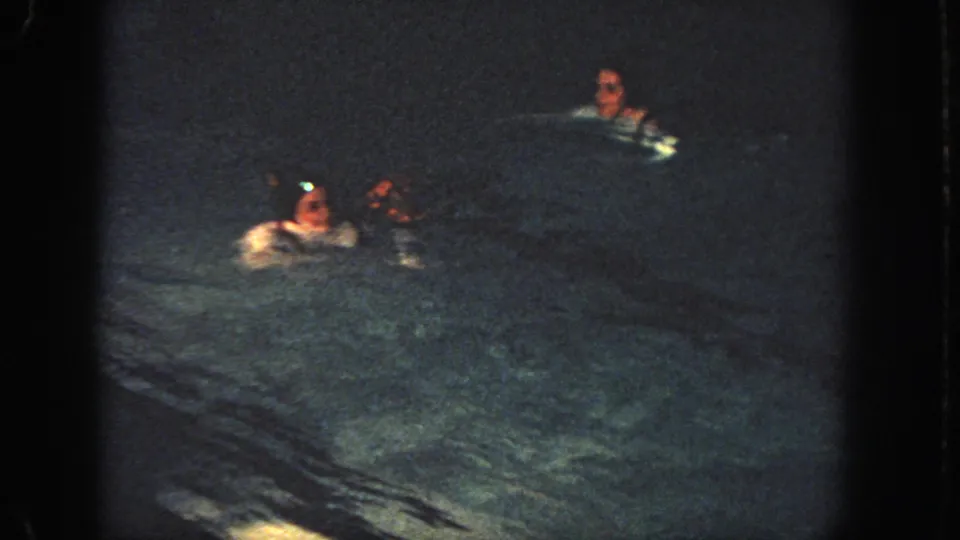 1951 Atlanta 8mm frame showing multiple swimmers in a dark pool at night, with soft focus and visible film grain.