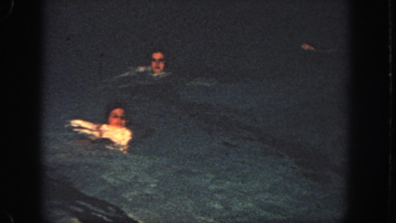 Two swimmers are visible in dark pool water at night.