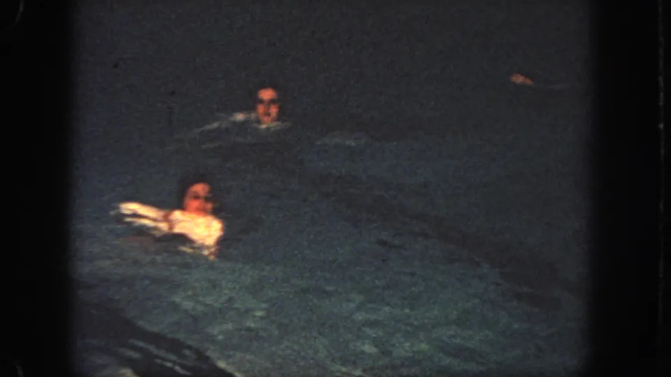1951 Atlanta home-movie frame with two swimmers separated across a dimly lit nighttime pool.