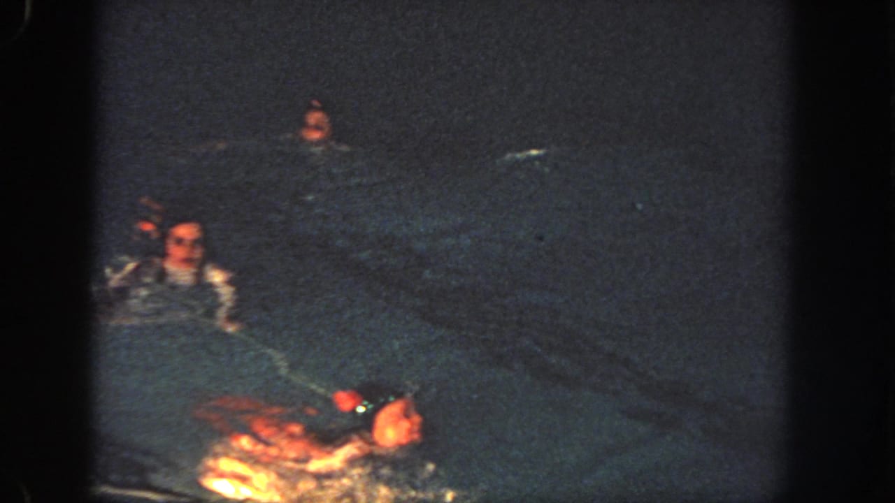1951 Atlanta home-movie frame with several swimmers spread through a dark nighttime pool, seen in grainy 8mm color.