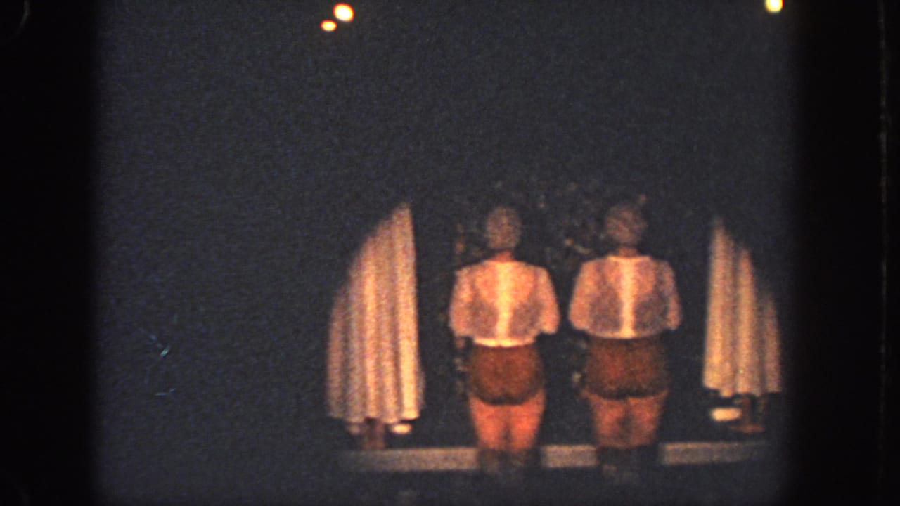 Two women in light tops and brown shorts stand on a dim Atlanta stage in this 1951 8mm home-movie frame.