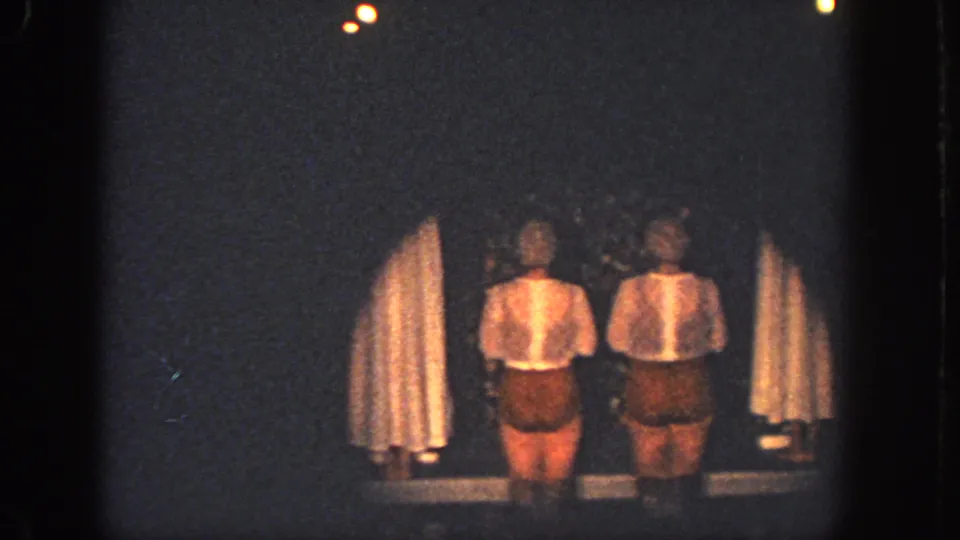 Two women in light tops and brown shorts stand on a dim Atlanta stage in this 1951 8mm home-movie frame.