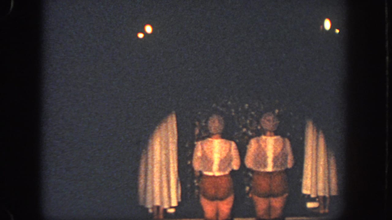 The 1951 Atlanta home-movie frame shows two women on a dark stage, framed by curtains and small overhead lights.