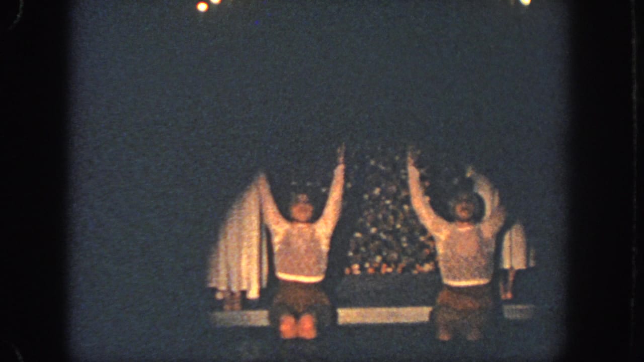 Two performers kneel or jump with arms raised on a dimly lit stage.