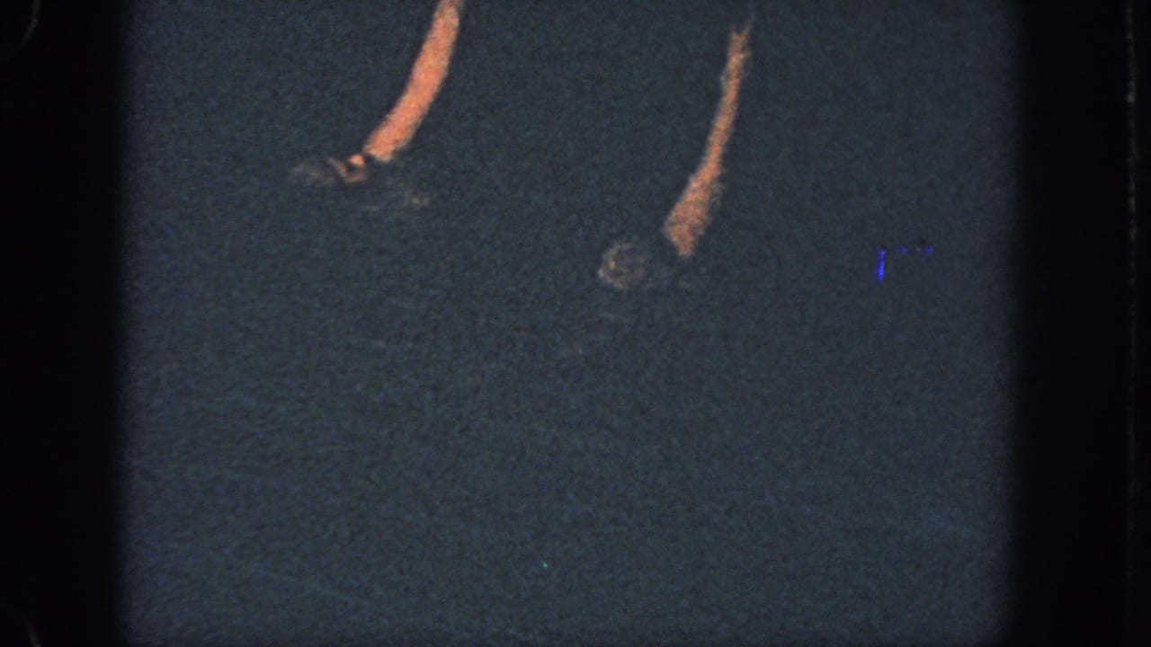 1951 Atlanta 8mm frame showing dim pool water with partial synchronized swimmers and raised arms under low light.