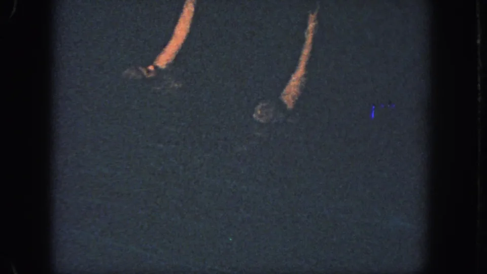 1951 Atlanta 8mm frame showing dim pool water with partial synchronized swimmers and raised arms under low light.