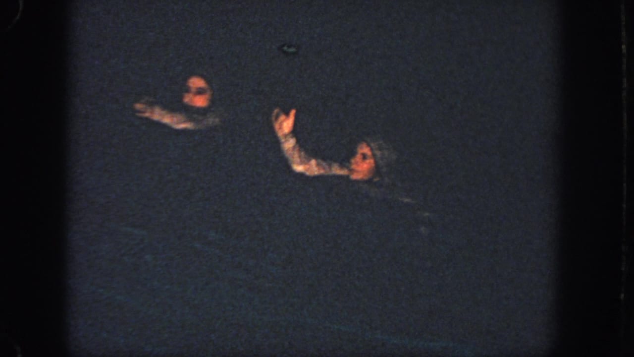 Two swimmers in dark water raise their arms during a nighttime routine.