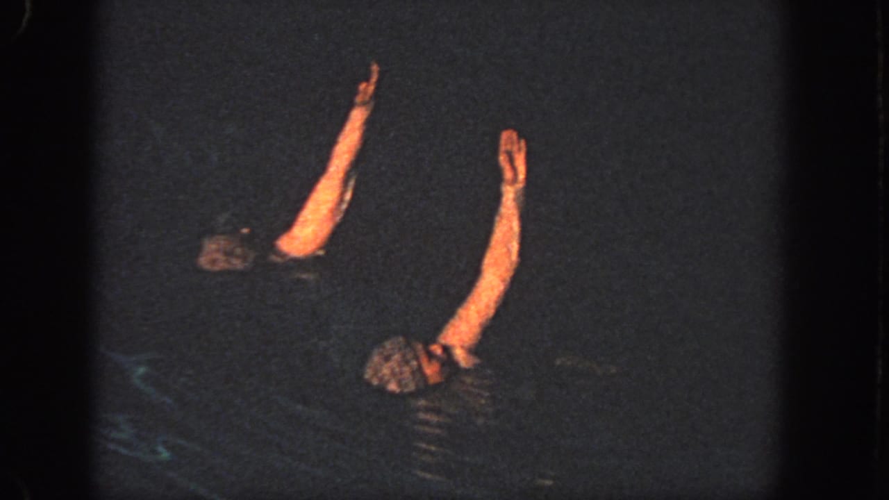 Two swimmers float apart in dark water with both arms extended upward.