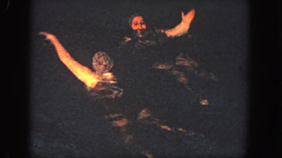 The 1951 Atlanta home-movie frame shows two synchronized swimmers facing one another as an arm sweeps across the dark pool surface.