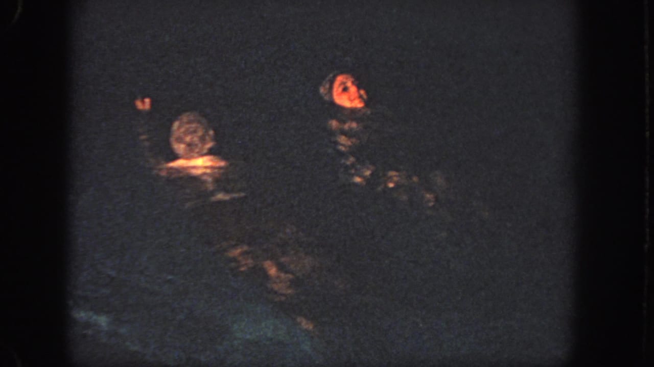 1951 Atlanta 8mm frame showing two swimmers in a dim pool, with warm light catching one face and raised hand.
