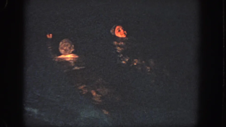 1951 Atlanta 8mm frame showing two swimmers in a dim pool, with warm light catching one face and raised hand.