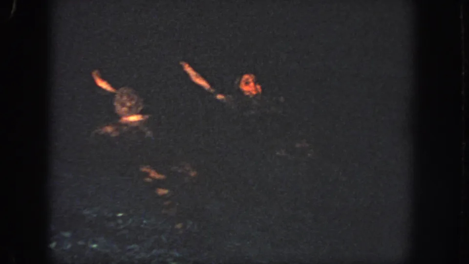 1951 Atlanta 8mm frame showing two swimmers mid-routine, their arms and faces briefly lit against dark pool water.
