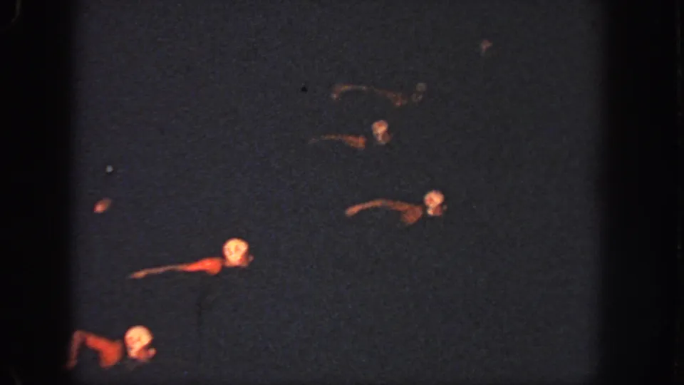 1951 Atlanta home-movie frame showing swimmers spread across dark nighttime pool water, one red-toned suit or float standing out.