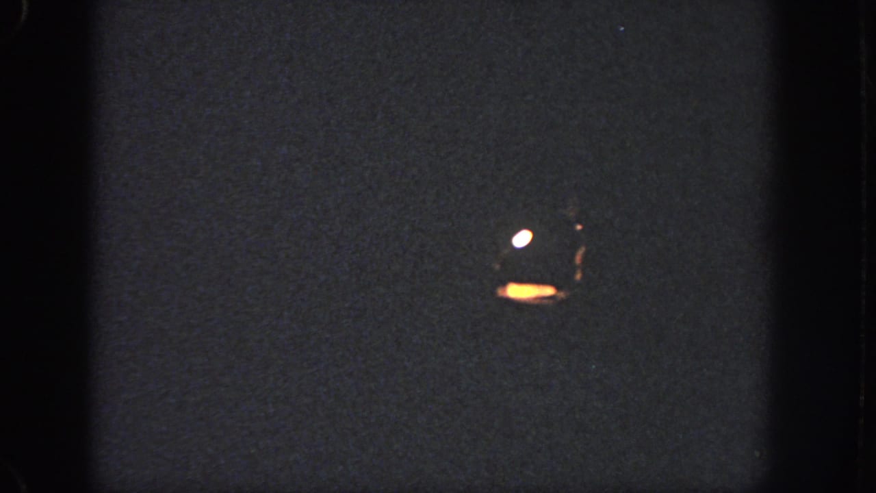 Dark pool surface with small bright reflections or flare marks in a low-exposure 1951 Atlanta 8mm frame.