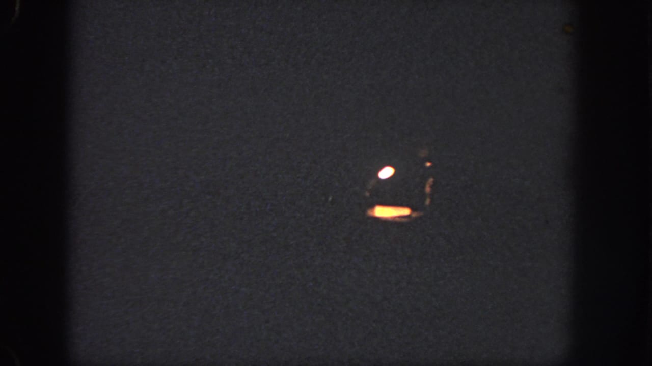 1951 Atlanta 8mm frame showing a dark projected surface with a small orange glow, white reflection, grain, and soft frame edges.