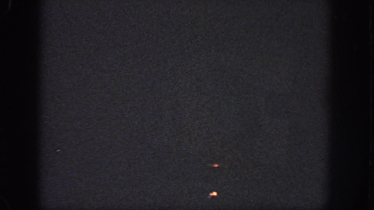 1951 Atlanta 8mm frame of a dark projected surface with small orange marks, visible grain, soft exposure, and film edge shadows.