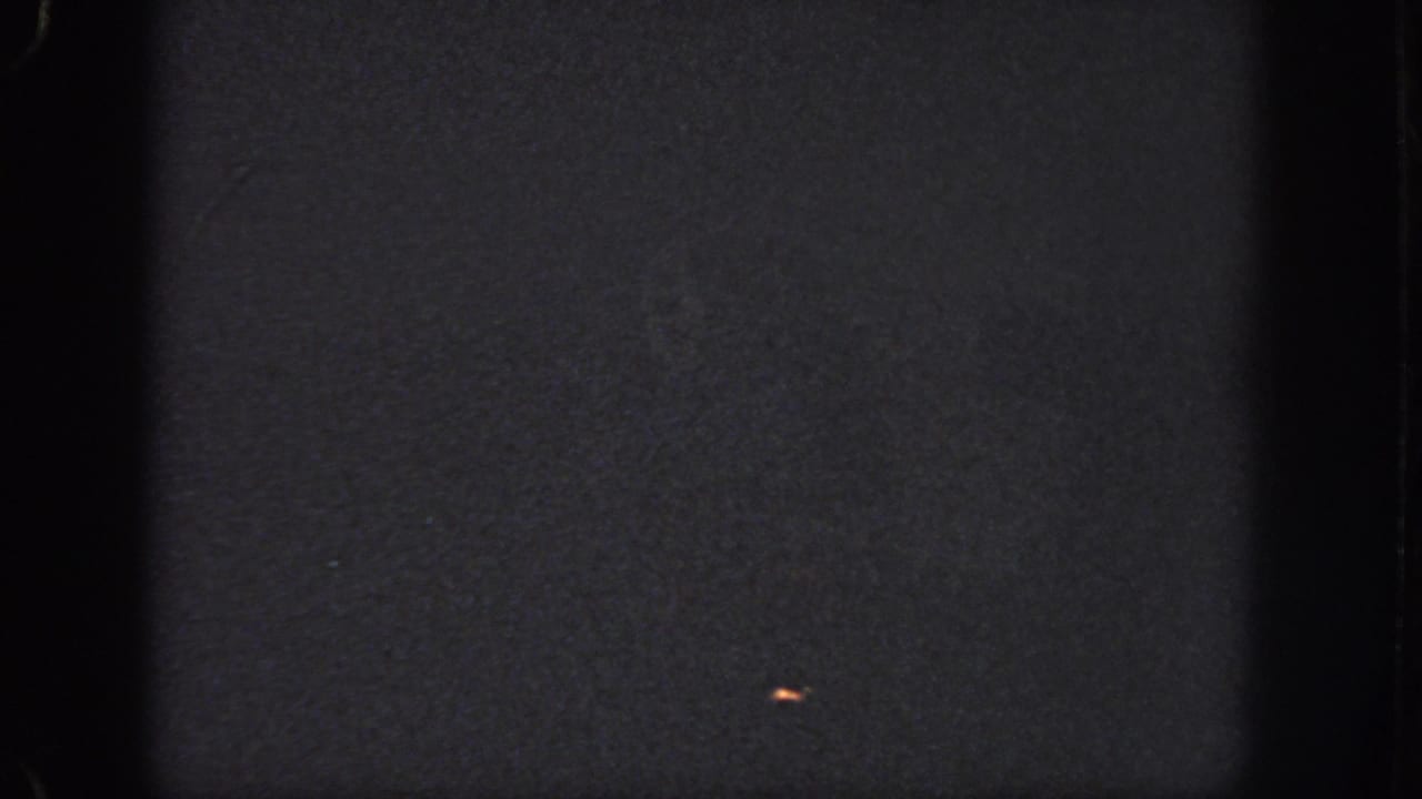 Dark Atlanta 1951 8mm frame with visible gate shadows, grain, and a small orange light-like speck on the right side.