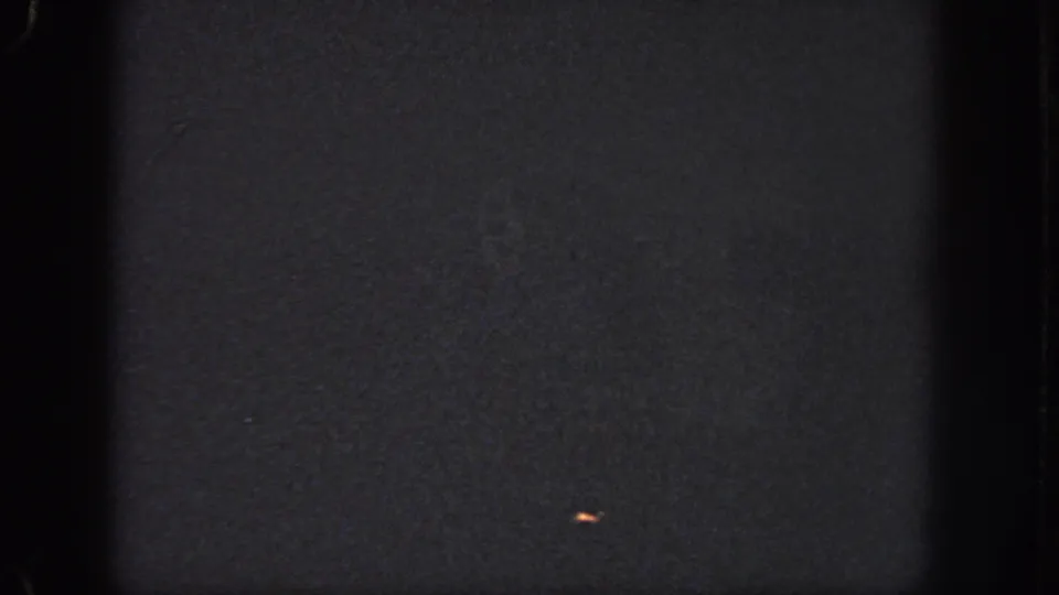 Dark Atlanta 1951 8mm frame with visible gate shadows, grain, and a small orange light-like speck on the right side.