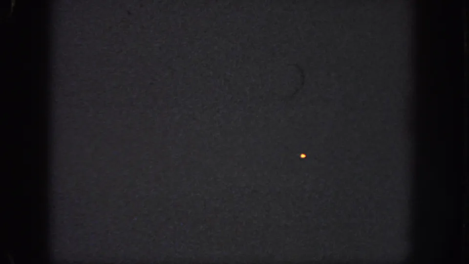 Underexposed 1951 Atlanta 8mm frame showing a small orange speck, heavy grain, dark gate edges, and no visible subjects.