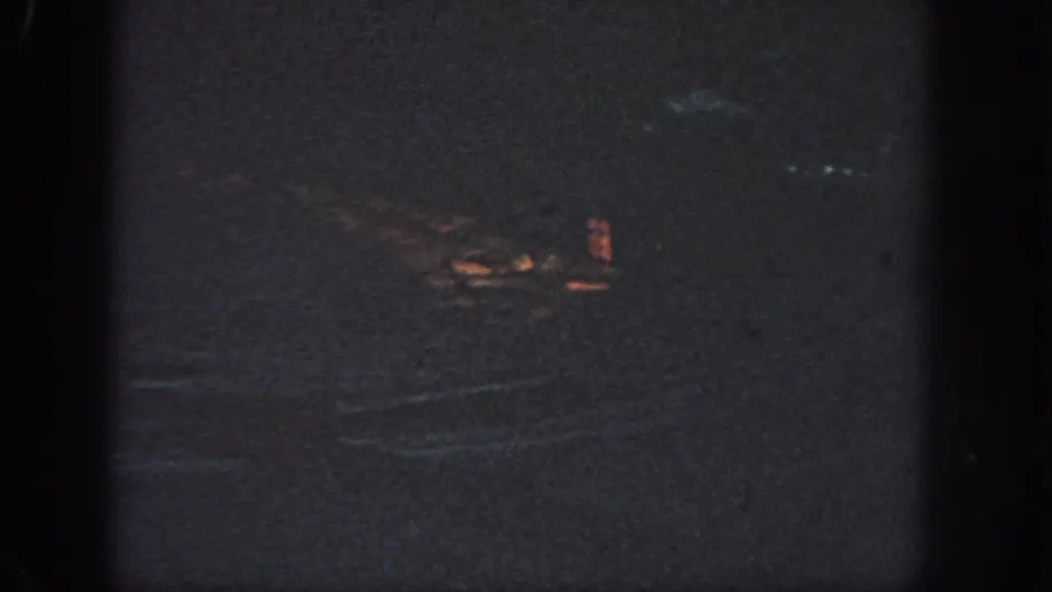 Atlanta 1951 8mm night-water frame with a small orange glowing area and dim reflections on a dark surface.