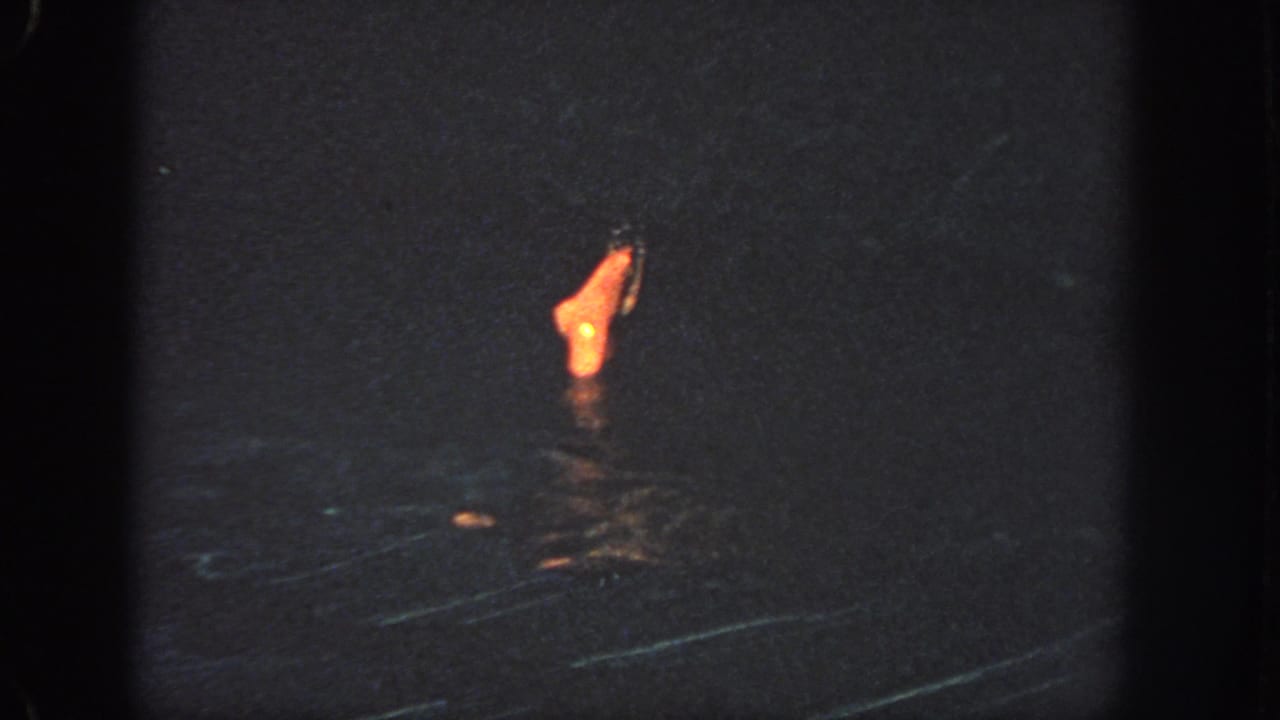 A swimmer's foot or lower leg breaks the surface of dark water under warm light.