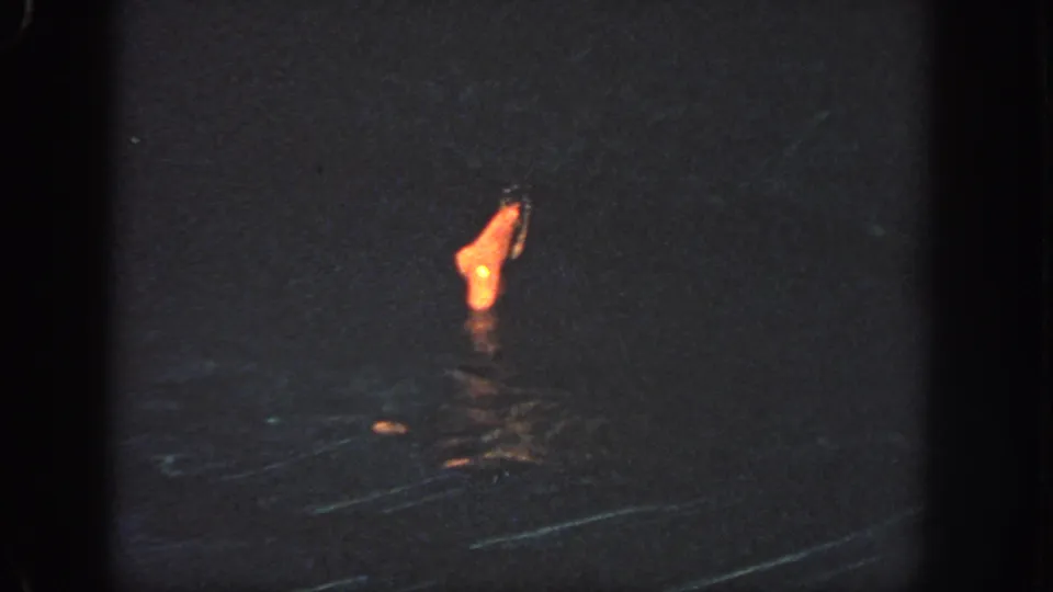 1951 Atlanta 8mm frame showing a swimmer partly submerged in dark water, with a foot or lower leg lit by a warm orange source.