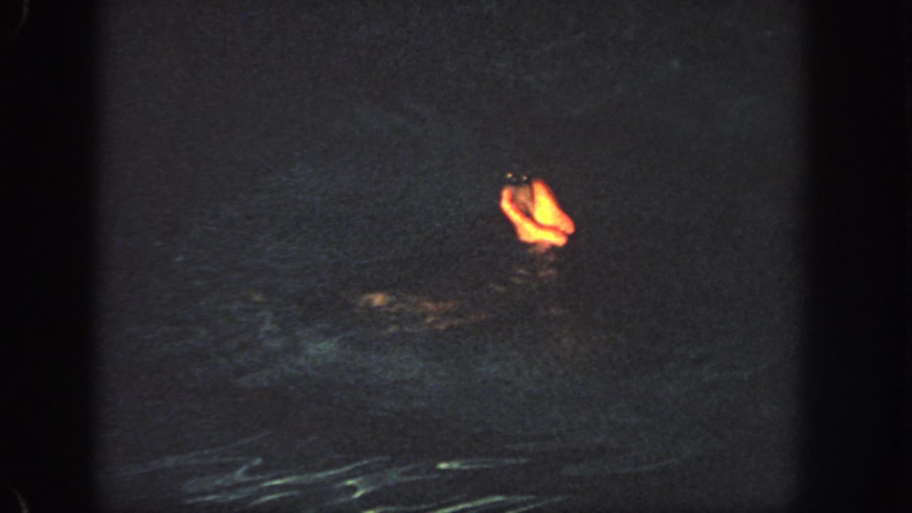 A lit foot or lower leg appears above dark rippling water in a low-light frame.