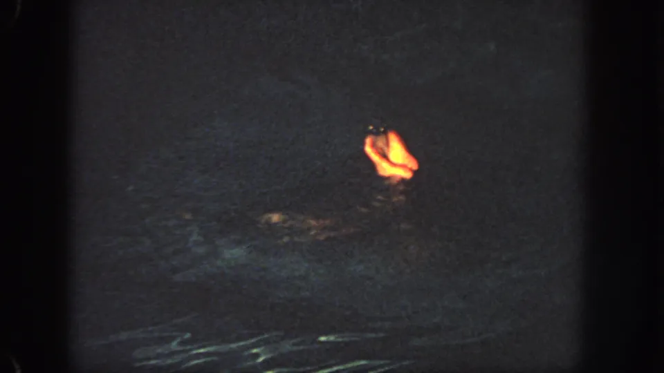 1951 Atlanta home-movie frame with a swimmer mostly hidden by dark water as a warm-lit foot or lower leg rises near the surface.