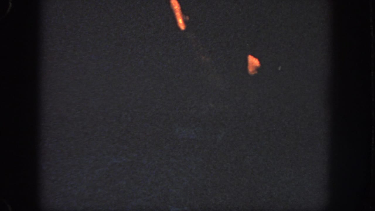 1951 Atlanta 8mm frame where the swimmer is mostly obscured, with small warm-lit portions visible against black water.